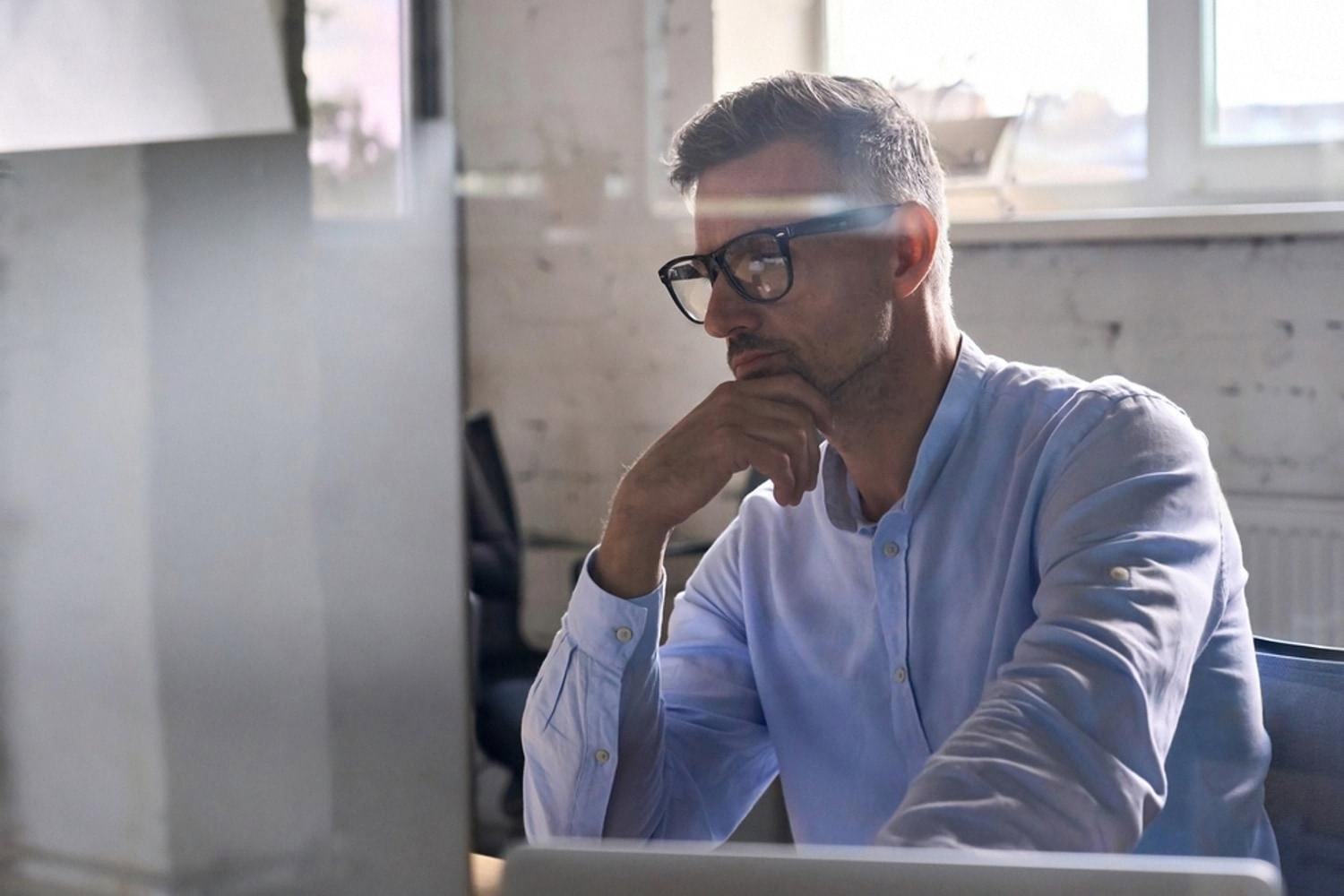 Male employee in glasses working at a desktop computer in a bright office