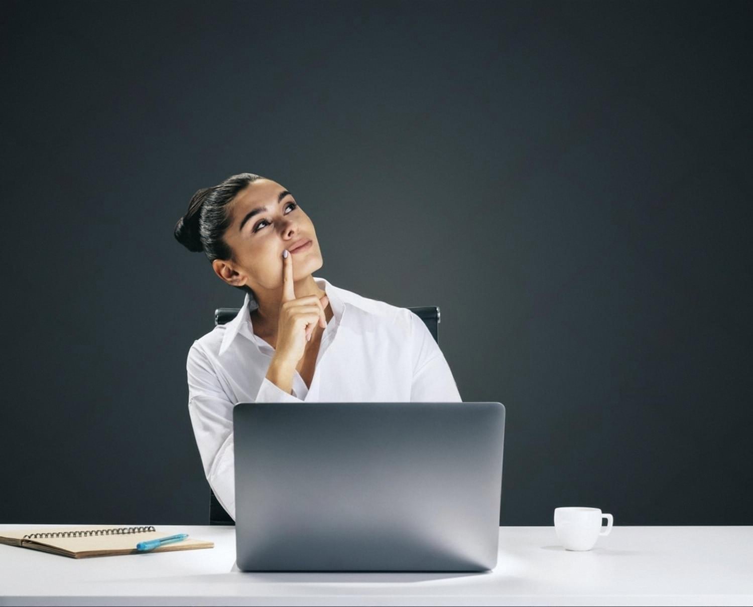 Female employee sitting at a white desk with a laptop, thinking about work